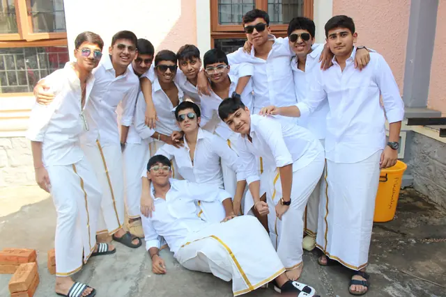 A group of boys in white shirts and veshti posing together in the sun