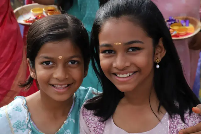 Two girls with tilak on their foreheads smiling at the camera