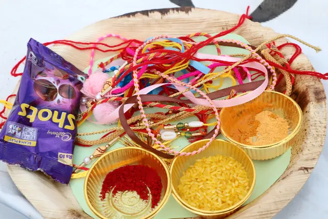 A leaf plate holding thread rakhis, red roli, yellow rice and chocolates