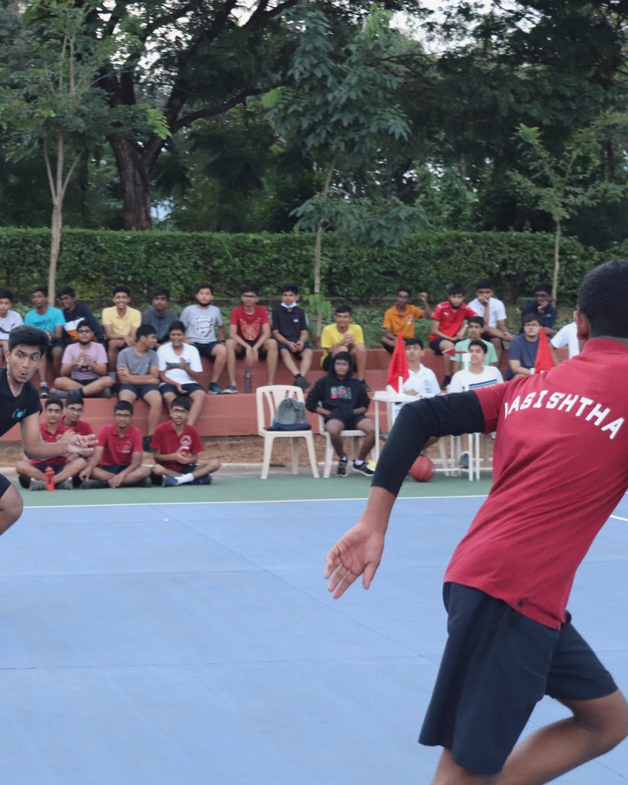 A CIRS student in a deep red house jersey printed Vasishtha, playing on the outdoor basketball court