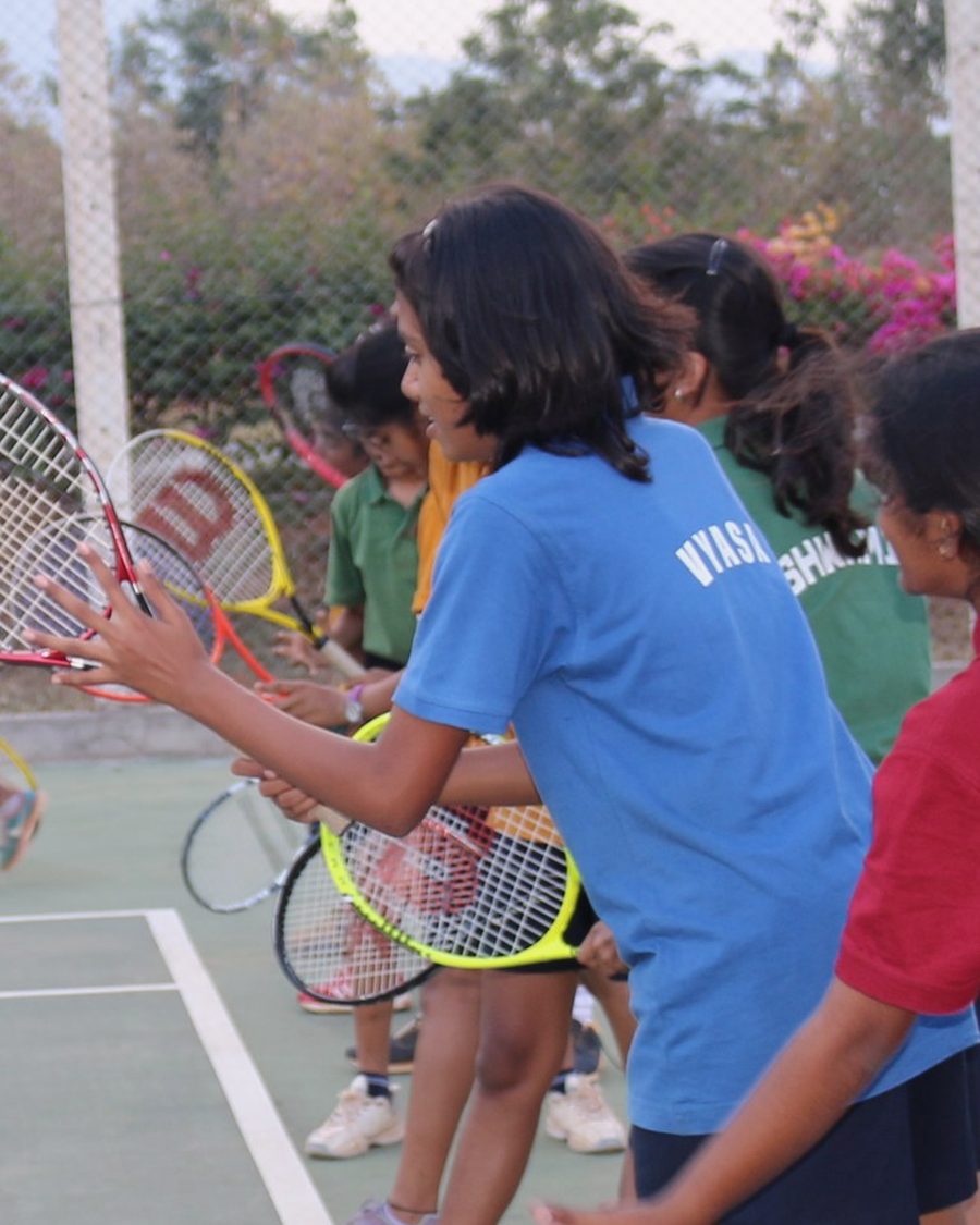 A CIRS student in a blue house shirt printed Vyasa, waiting to return at a tennis session