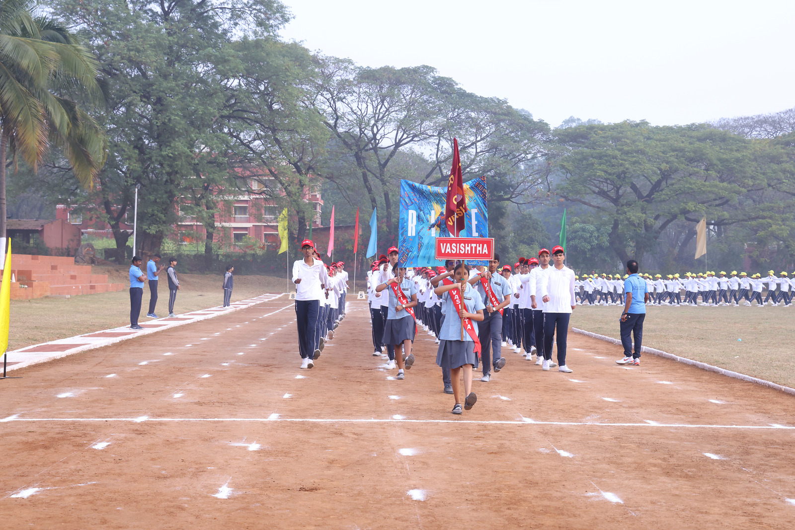Vasishta students marching behind their named red house banner