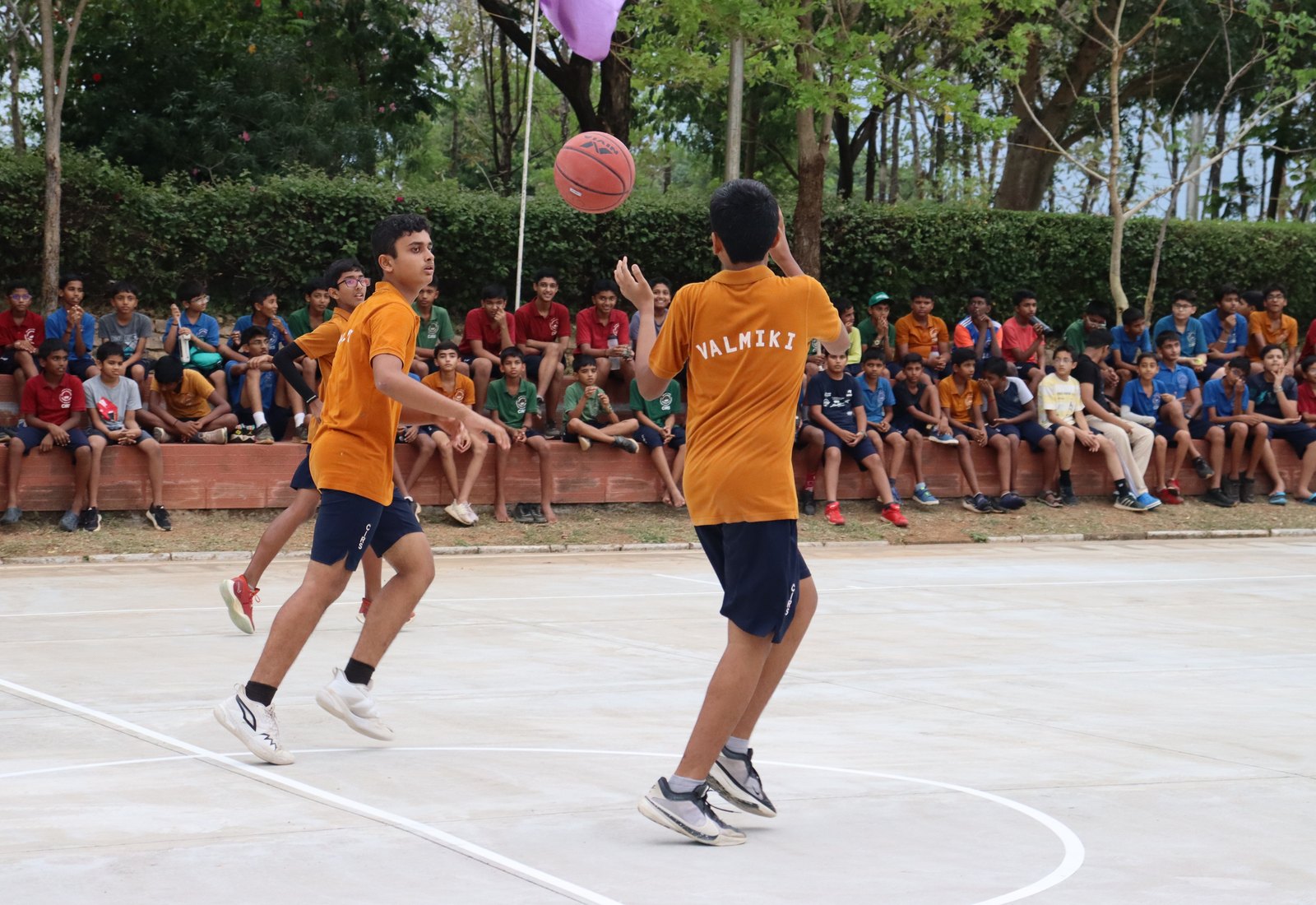Valmiki players passing a basketball, with the house name visible on yellow shirts