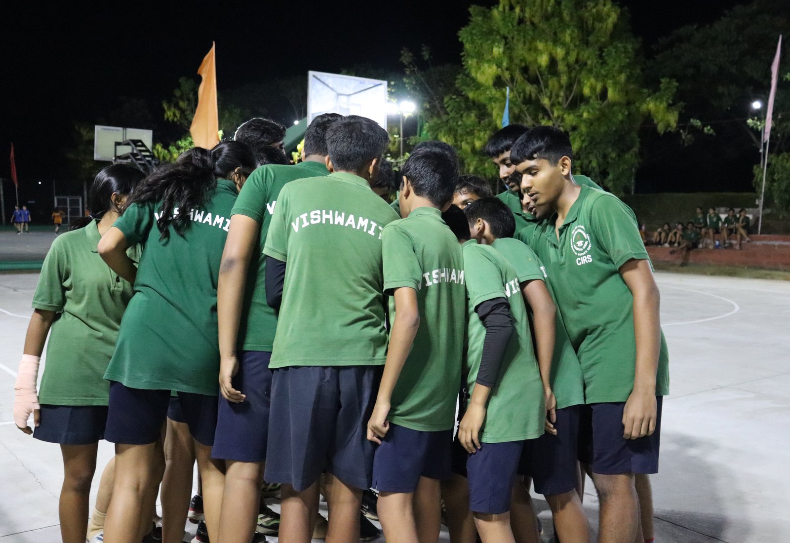 Vishwamitra basketball players huddling in green shirts bearing the house name