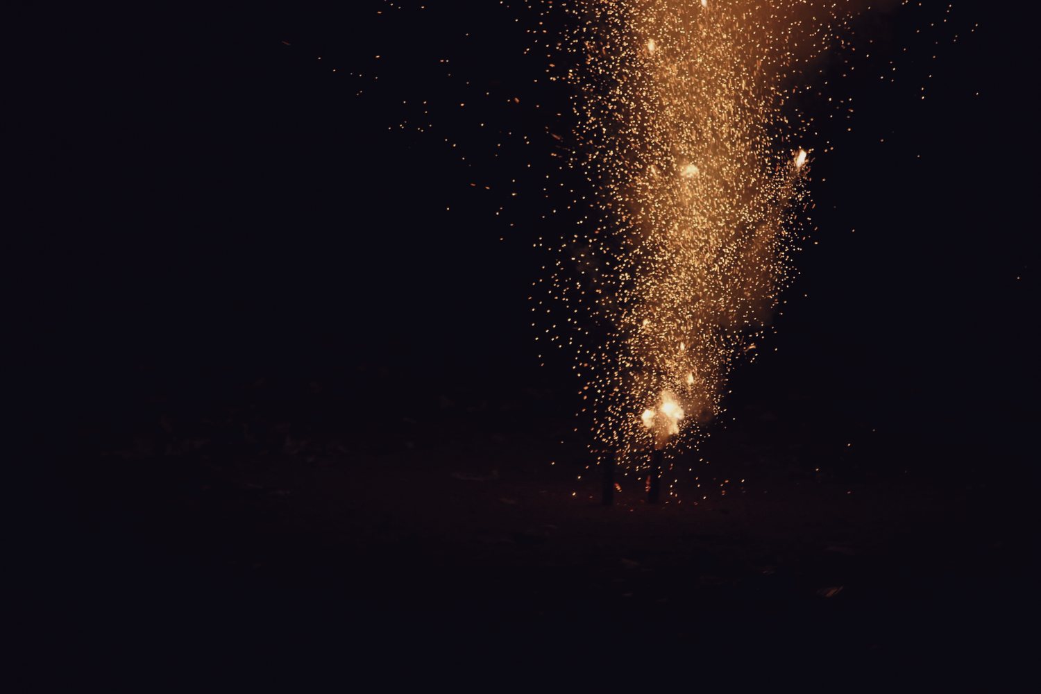 A fountain of sparks rising from the ground into the dark.