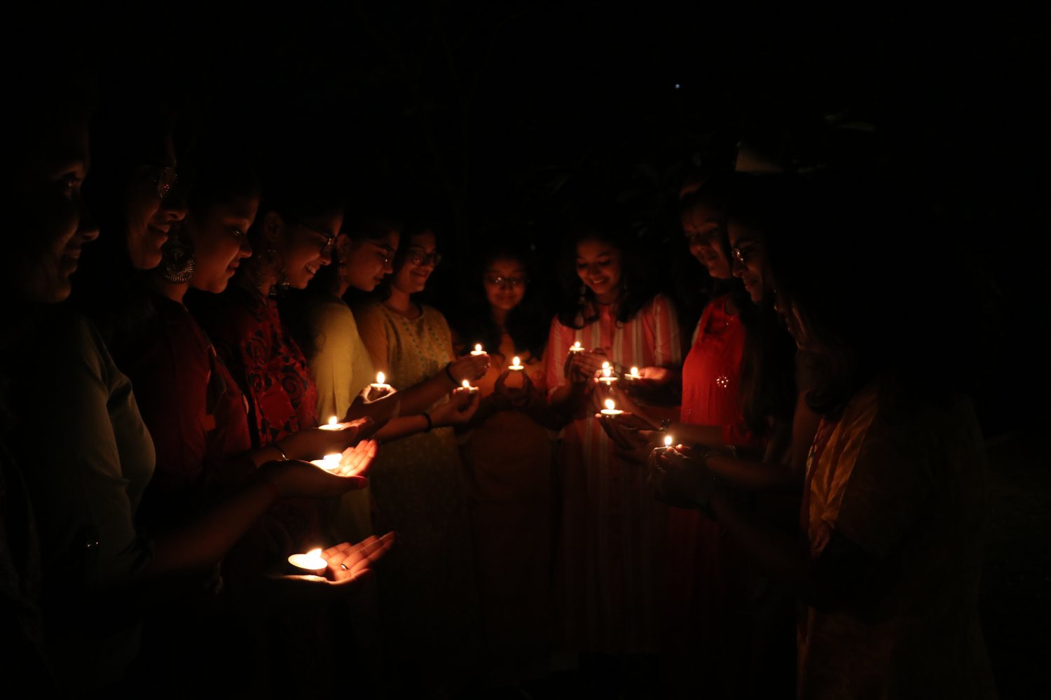 Students standing together in the dark, each holding a small lit lamp.