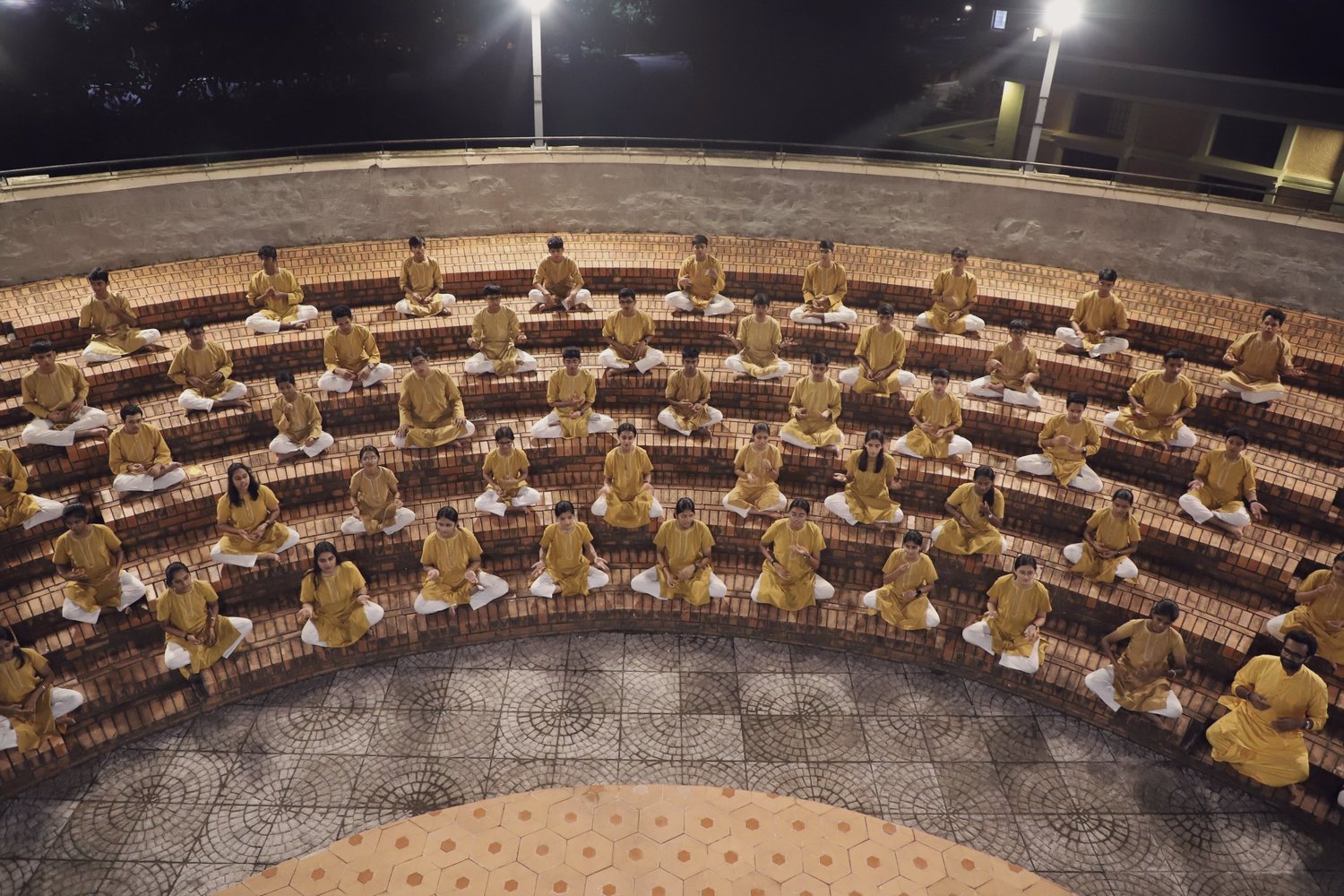 Students seated in the concentric brick rings of the CIRS amphitheatre after
dark, under floodlights, during evening practice.