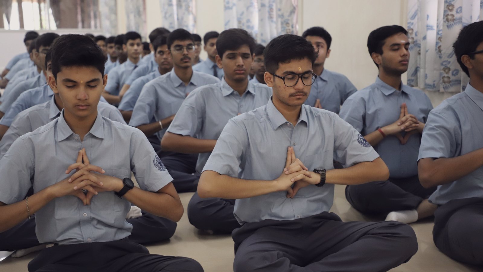 Students seated cross-legged with their palms joined at morning prayer