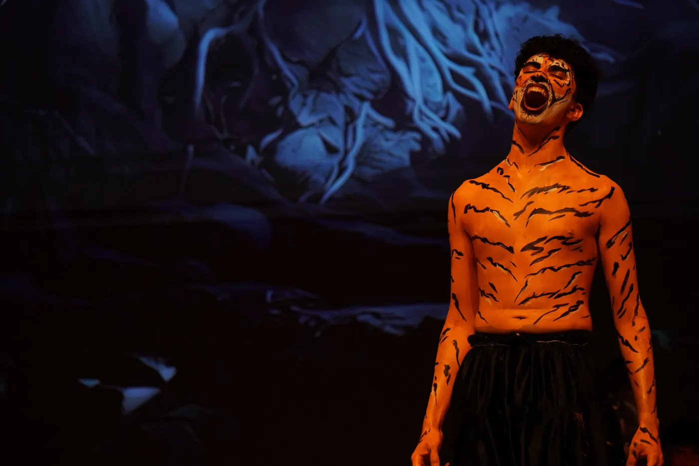A CIRS student in tiger face paint and costume performing on stage during Masquerade
