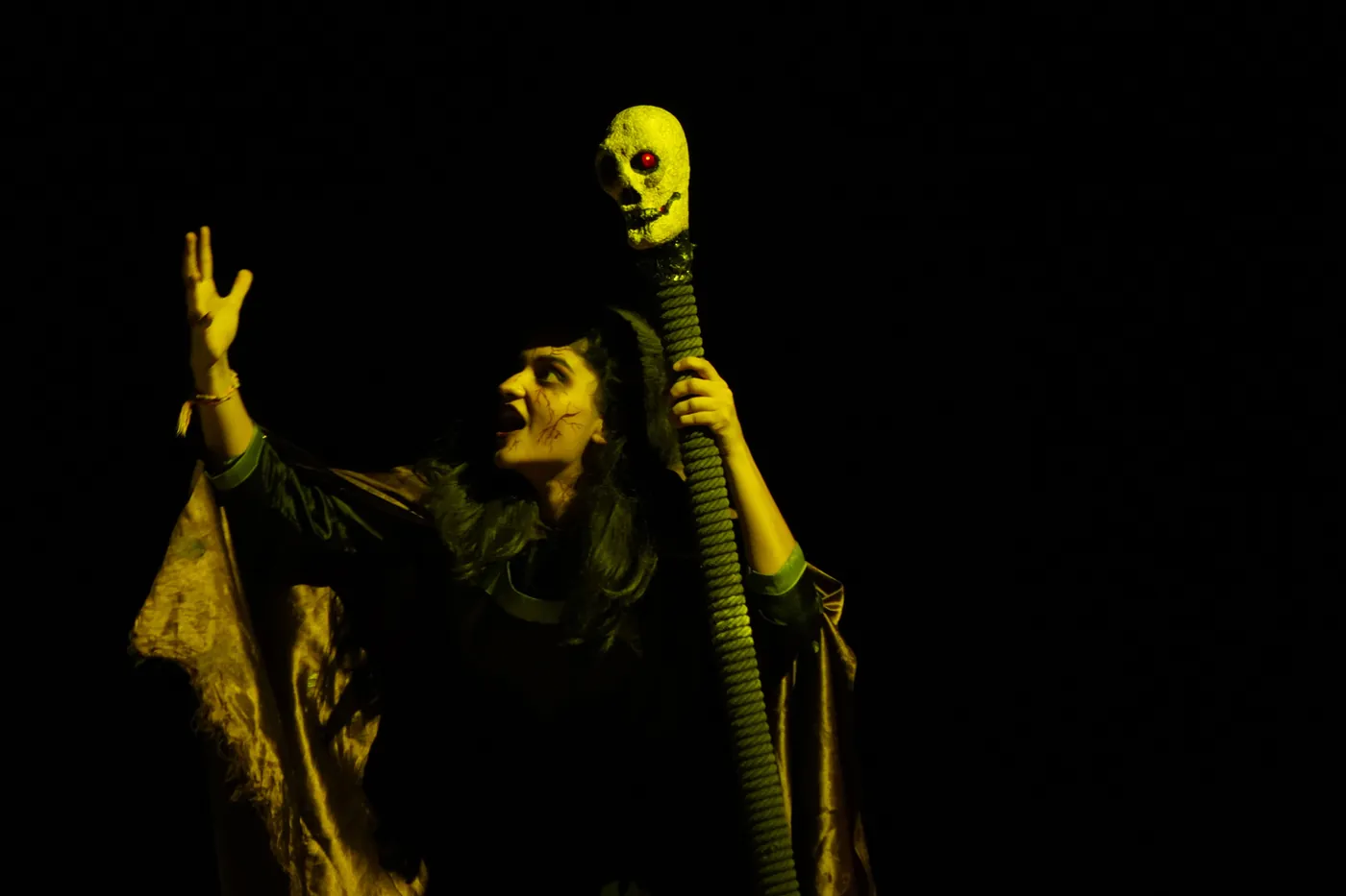 A performer with a staff under yellow stage light during Masquerade