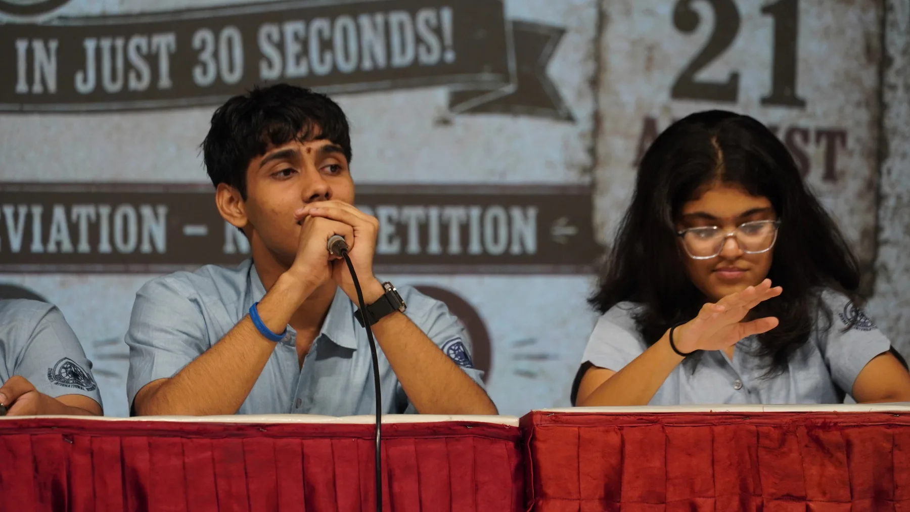 Two students at a table with microphones before a backdrop that reads In just 30 seconds