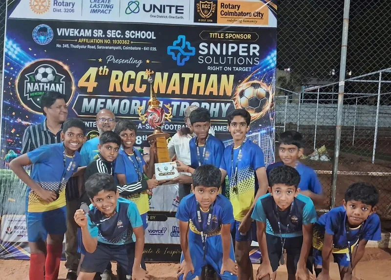 Boys in blue and yellow kits gathered before a banner for the 4th Nathan Memorial Trophy football tournament