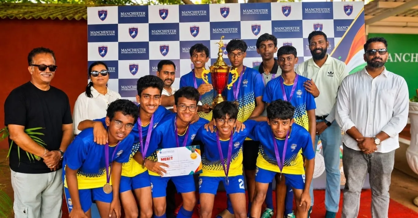 A football team in blue and yellow kits wearing medals and holding a trophy, with adults standing beside them