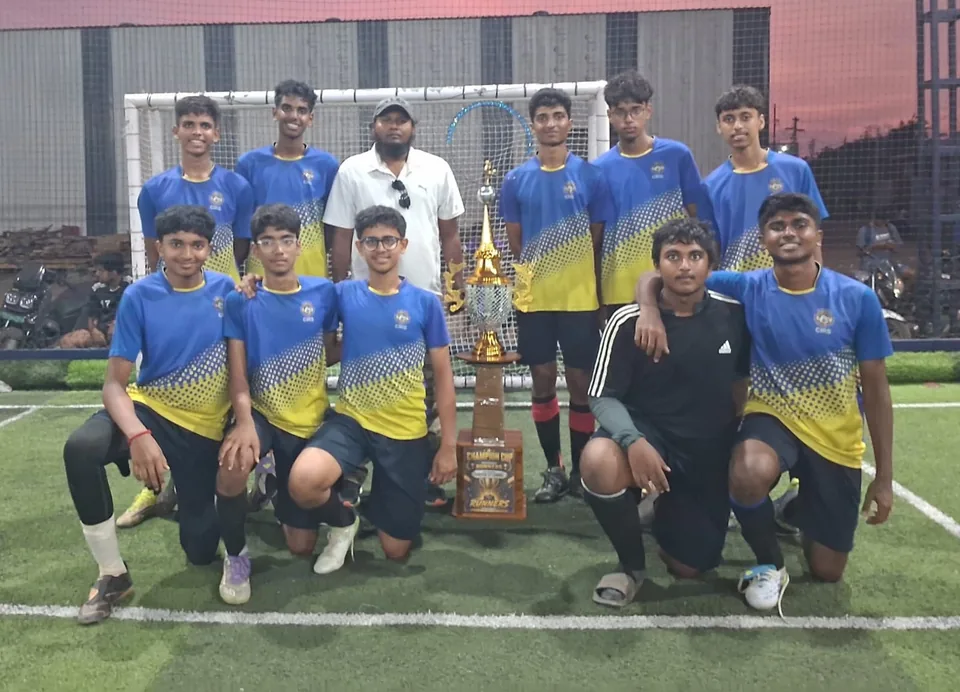 A football team in yellow and blue kits kneeling beside a trophy on a pitch