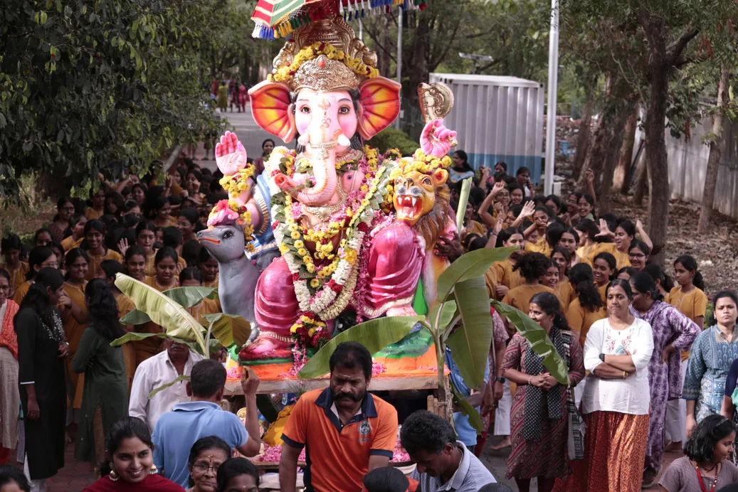 A decorated Ganesh murti carried through a crowd of students and staff