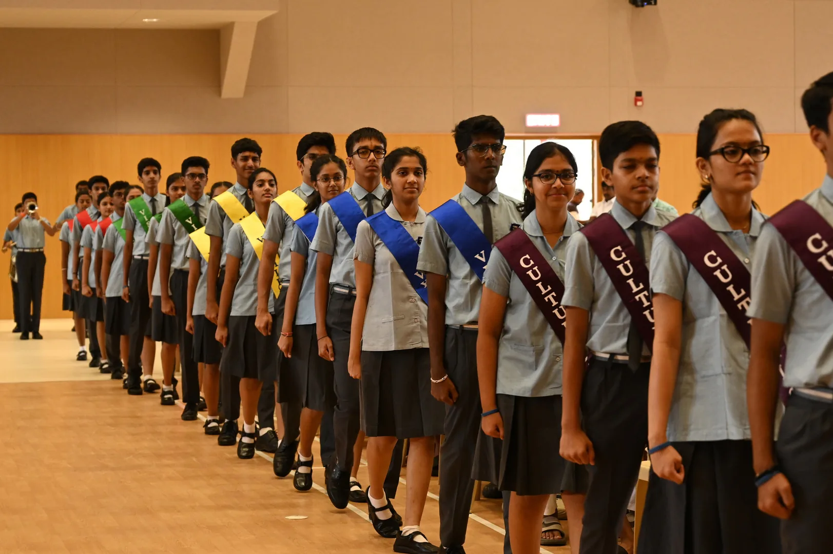 Students in school uniform wearing sashes standing in a long line in a hall