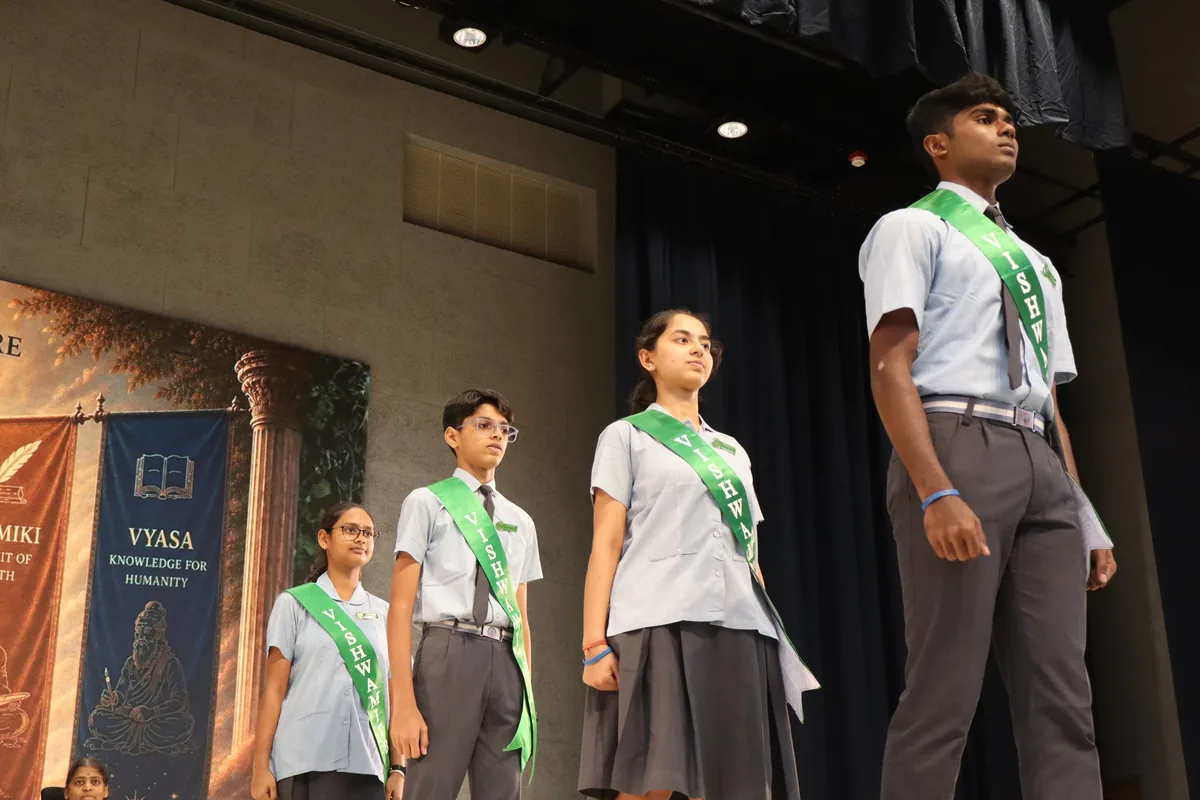 Three students wearing green sashes on a stage before a Vyasa banner
