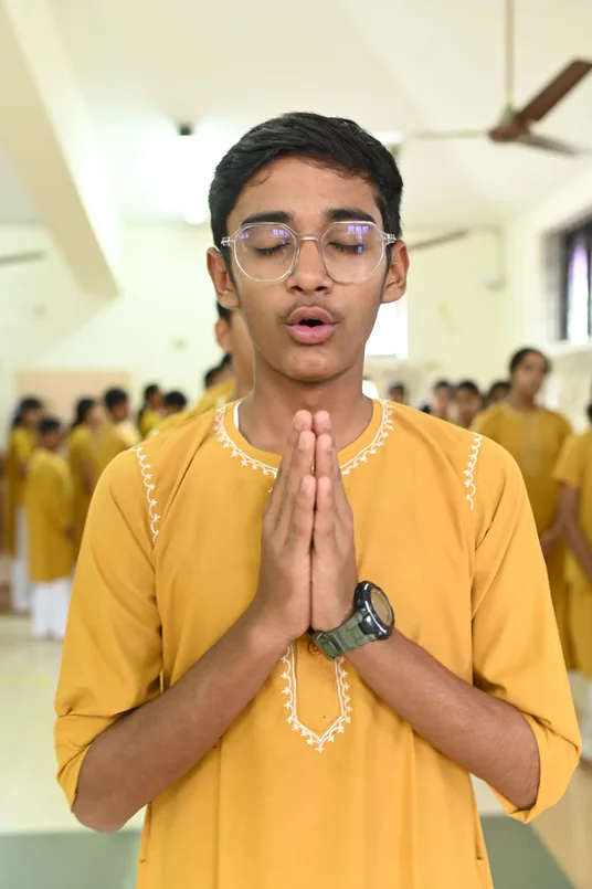 A student in a yellow kurta with palms joined