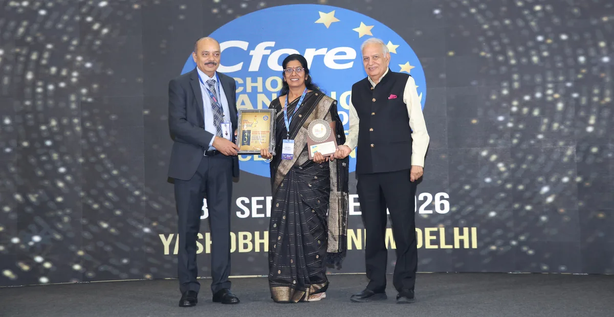 A woman in a sari holding a trophy on the stage of the Cfore School Rankings 2026 event, between two men