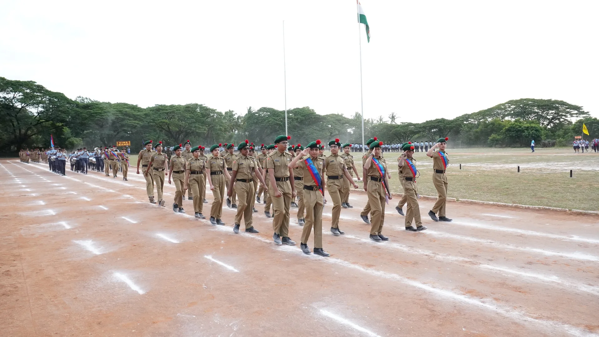 Uniformed cadets marching across a parade ground under a flag