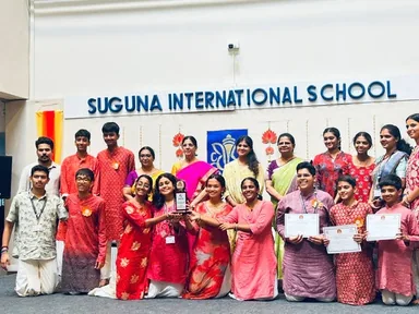 Students and adults, several holding certificates, standing beneath a Suguna International School sign