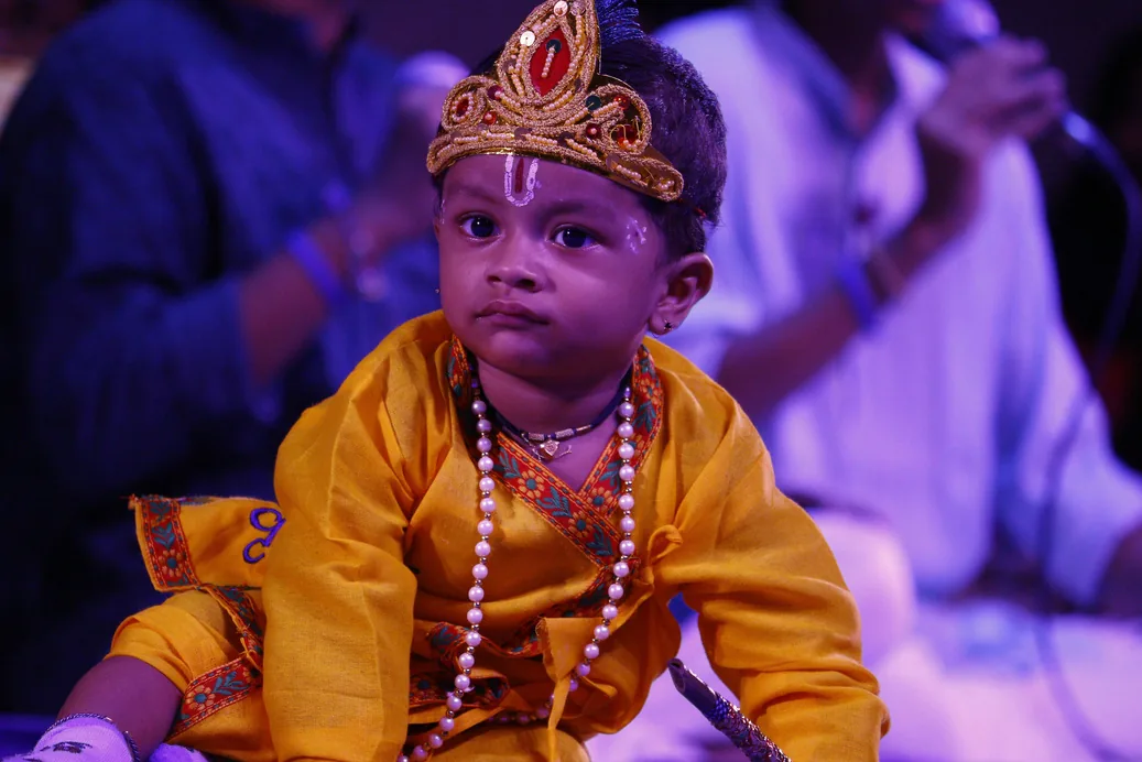 A small child dressed as Krishna in a crown and a pearl necklace