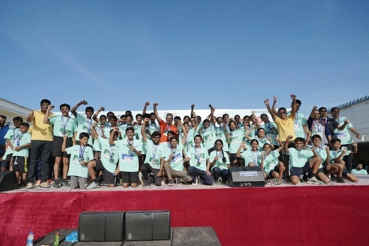 A large group of students in matching light-green shirts on a stage after the Kangeyam Marathon