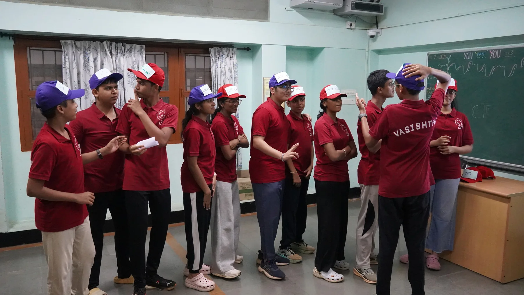 A team of students in maroon shirts standing in a line in a classroom