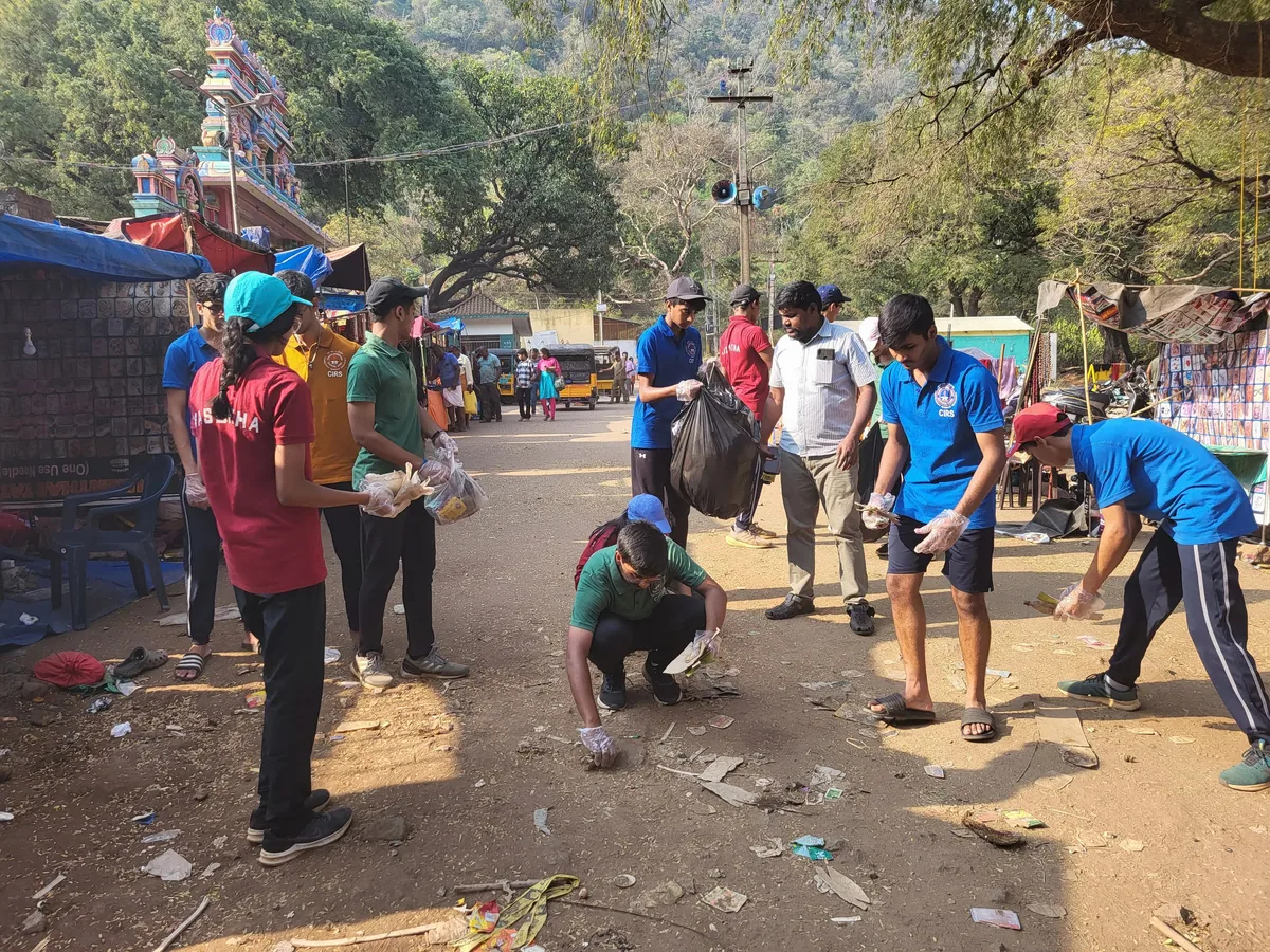 Students and staff picking up litter on the ground outside a temple