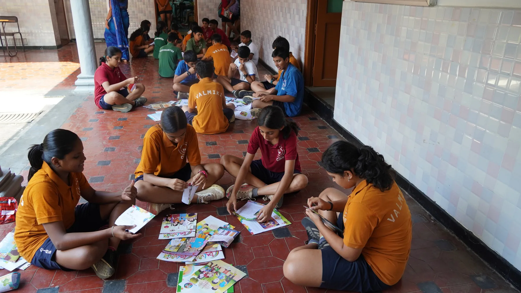 Students in mustard kurtas seated on the floor with sheets of paper