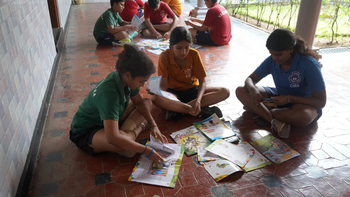 Students seated on a tiled floor sorting notebooks and papers