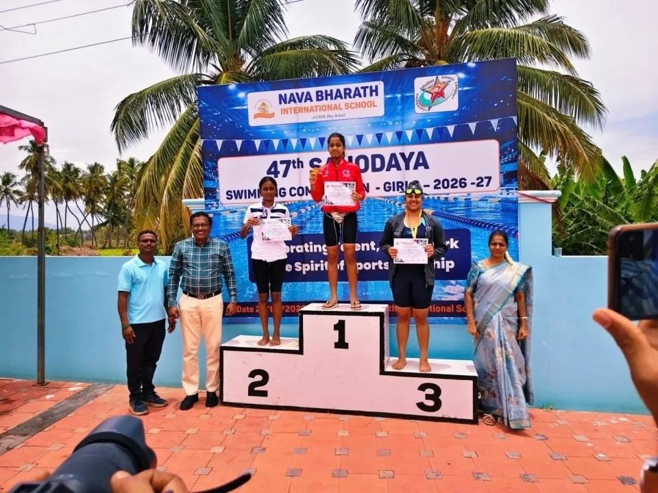 A girl on the winners’ podium at the 47th Sahodaya Swimming Competition for girls, with officials standing beside it