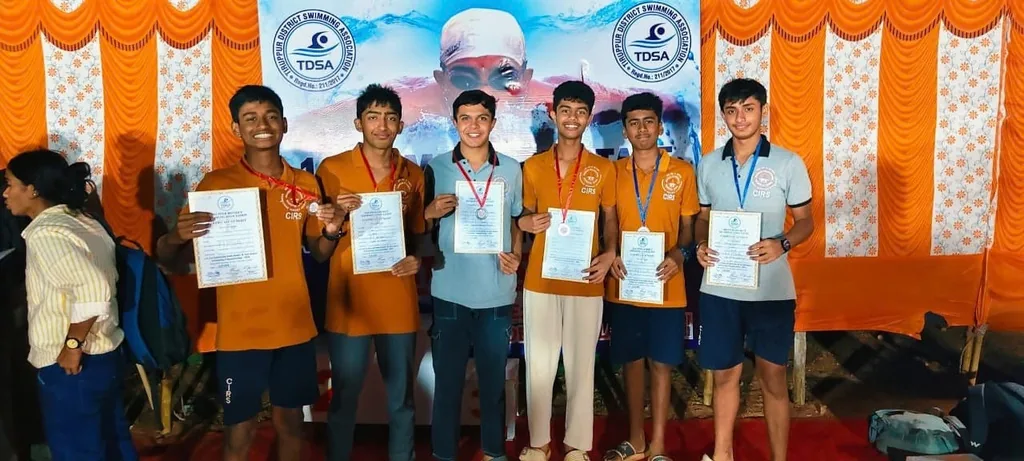 Boys in orange shirts holding certificates in front of a banner