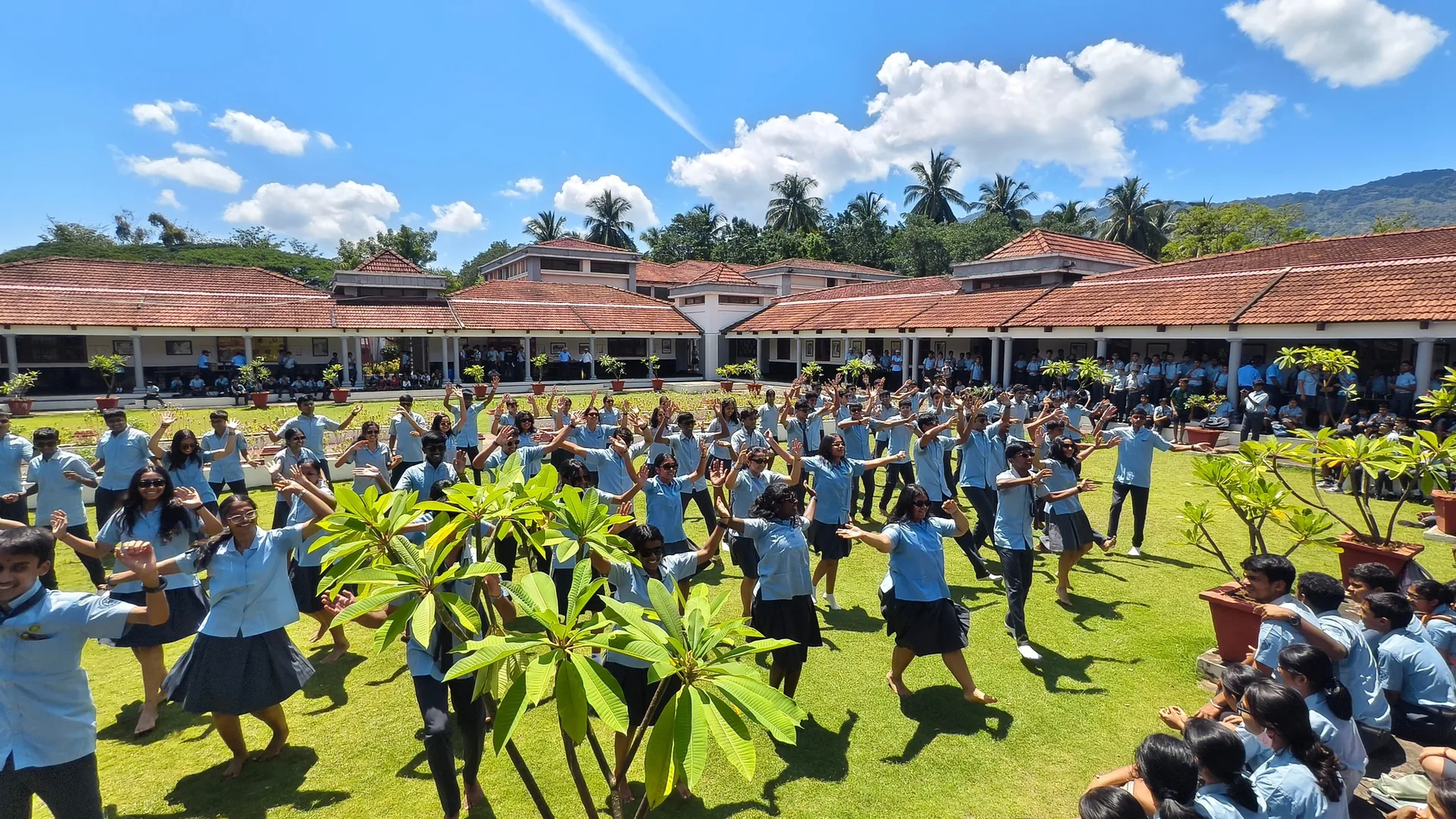 Students in blue and grey standing in formation on a lawn in front of the school buildings