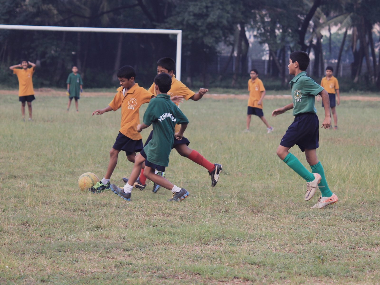 Young CIRS footballers in green and amber shirts chasing the ball on the school field