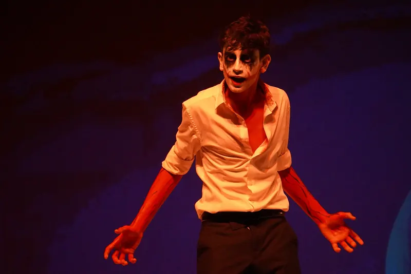 An actor in white skull face paint under orange light, hands open
