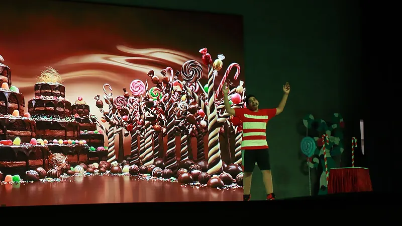 A lone actor in a striped shirt beside a projected landscape of chocolate and candy canes