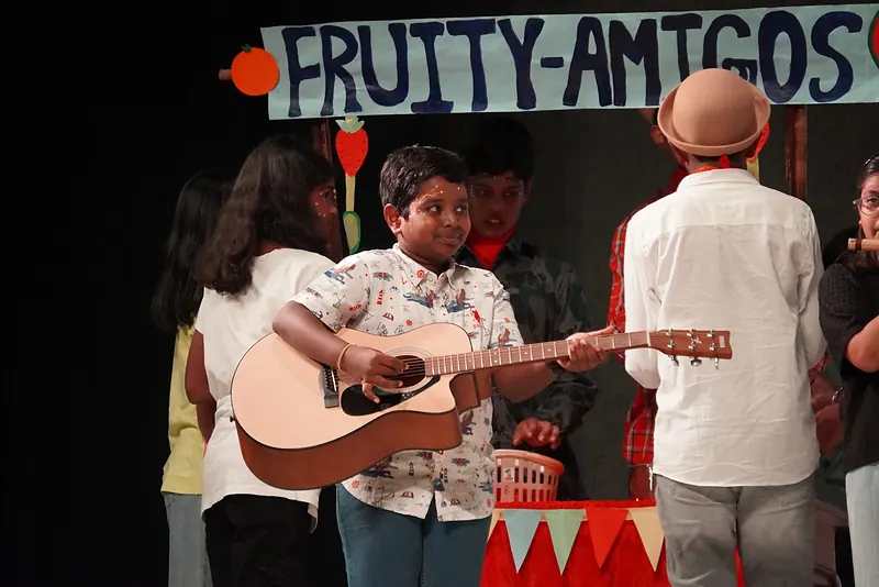 A boy playing a guitar at a stall beneath a hand-painted sign
