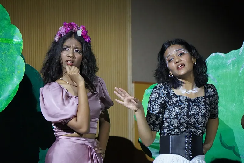 Two performers among giant painted leaves, one with flowers in her hair