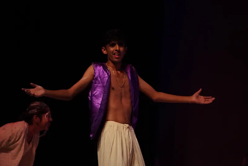 An actor in a purple waistcoat with arms spread