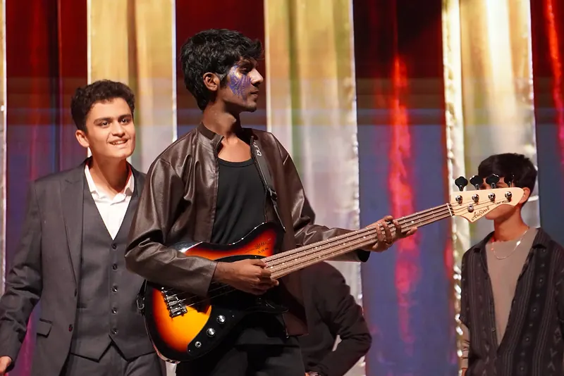 An actor with a bass guitar between two others before striped curtains